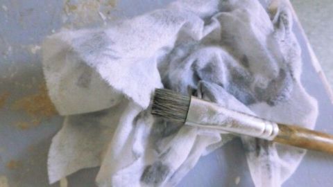 Ein Ölpflegetuch liegt zusammen mit einem Pinsel auf einem leicht verschmutzten Tisch, bereit für den Einsatz im Haushalt.