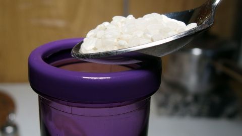 Thermoskannen oder Trinkflaschen mit Reiskörnern reinigen. Eine Löffel mit Reinigungsmittel schwebt über einer Thermoskanne, während sie in einer Küche steht.