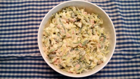 In einer weißen Schüssel liegt ein Lauchsalat mit Schinken, umgeben von einem karierten Tischdeckenmuster.