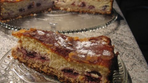 Eine Quark-Sahne-Kirsch-Torte mit Kokosgeschmack ist auf einem schönen Glasuntersetzer zu sehen. Ein Stück ist auf einem weiteren Teller platziert.