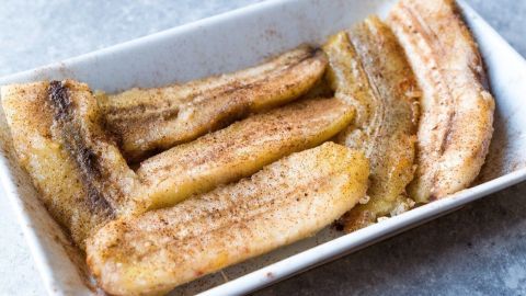 Reife Bananen werden in einer weißen Schale gezeigt, leicht gebräunt und mit Zimt bestäubt, bereit für den Verzehr.