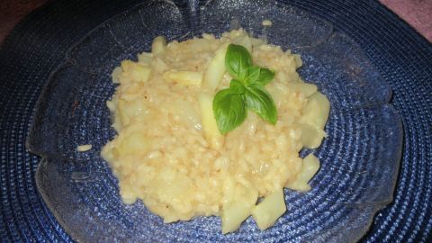 Ein cremiges Spargel-Risotto liegt auf einem blauen Teller, garniert mit frischem Basilikum, umgeben von einem schlichten Hintergrund.