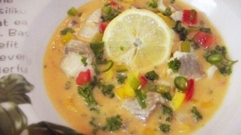Eine cremige Fischsuppe mit Seelachs, Paprika und frischen Kräutern, garniert mit einer Zitronenscheibe in einer Schüssel.