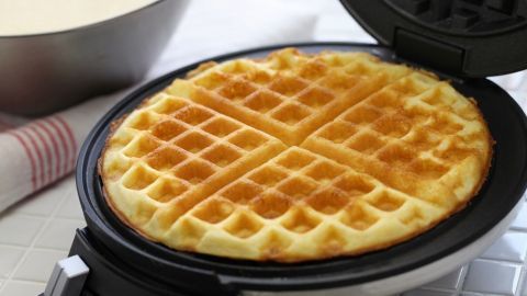 Eine frisch gebackene Waffel liegt in einem Waffeleisen, umgeben von einer Schüssel Teig. Genuss und Vorbereitung für lockere Waffeln.