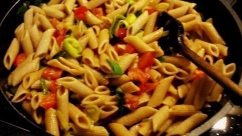 Eine bunte Gemüsepfanne mit Penne wird in einer Pfanne serviert, umgeben von frischen, geschnittenen Gemüsewürfeln.