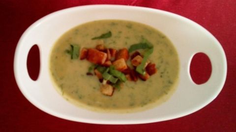 Eine cremige Bärlauch-Kartoffelsuppe wird in einer weißen Schüssel serviert, dekoriert mit knusprigem Speck und frischen Kräutern.
