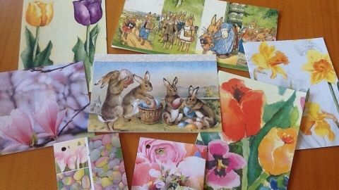 Bunte Grußkarten aus Servietten liegen auf einem Tisch und zeigen vielfältige Frühlingsmotive mit Blumen und Tieren.