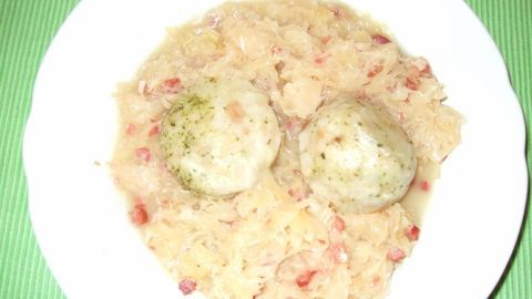 Ein Teller mit Schmackhaftem Speckkraut und zwei Klößen in einer hellen, cremigen Sauce auf einem grünen Untergrund.