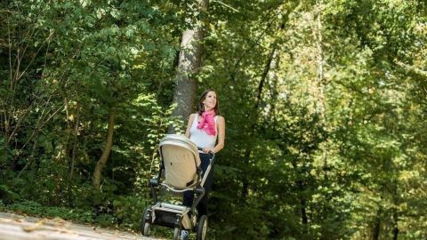 Ein Kind im Kinderwagen blickt zu den Eltern, während sie einen Waldweg in herbstlicher Umgebung entlanggehen.