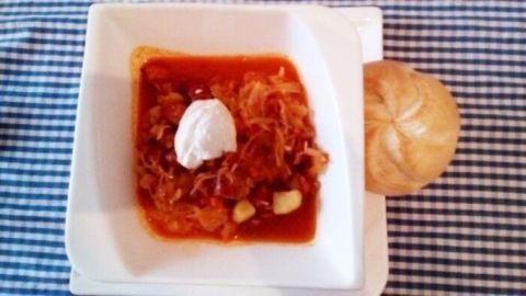 Ein rustikaler Sauerkrauttopf mit roter Sauce und einem Klecks Sahne wird appetitlich auf einem Teller serviert, daneben ein Brötchen.