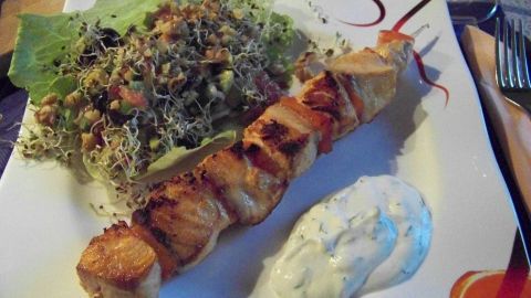 Gegrillter Lachsspieß liegt neben einem frischen Grapefruit-Avocado-Salat auf einem Teller, dazu Dip.