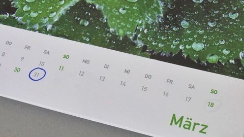 Ein Kalenderblatt für den Monat März zeigt das Datum an, während Wassertropfen auf einem grünen Blatt Hintergrund glänzen.