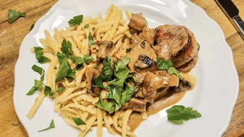 Eine Lende in Sahnesoße mit Spätzle und frischer Petersilie auf weißem Teller, auf hölzerner Tischplatte angerichtet.