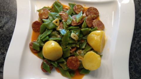 Scharfe grüne Bohnen sind in einer weißen Schüssel angerichtet, umgeben von Kartoffeln und einer würzigen Sauce.