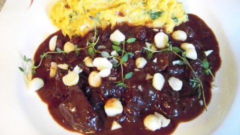 Ein appetitlicher Teller mit Wildschweingulasch, garniert mit Nüssen und Kräutern, neben einem cremigen Süßkartoffelstampf.