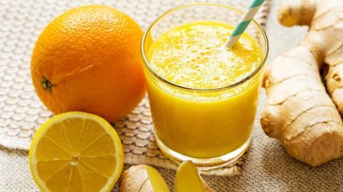 Ein frisch zubereiteter Ingwer-Shot steht in einem Glas, umgeben von Orange und Limette, auf einem strukturierten Untergrund.