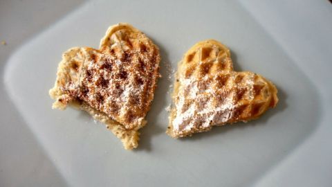 Herzförmige Waffeln liegen auf einem Teller und sind mit Puderzucker bestäubt, ideal zum veganen Backen ohne Eier.