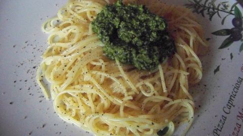 Spaghetti liegen auf einem Teller, bedeckt mit grünem Bärlauchpesto, umgeben von einer dekorativen Tellerkante.