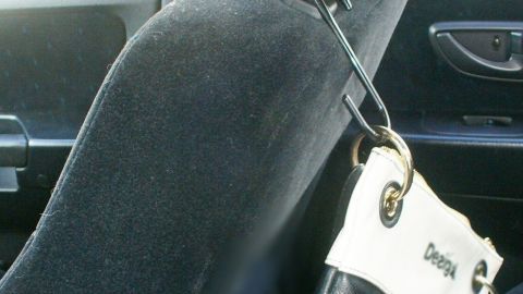 Eine Handtasche hängt am Kopfstützenpolster eines Autos, während der Innenraum dunkel und gepolstert ist.