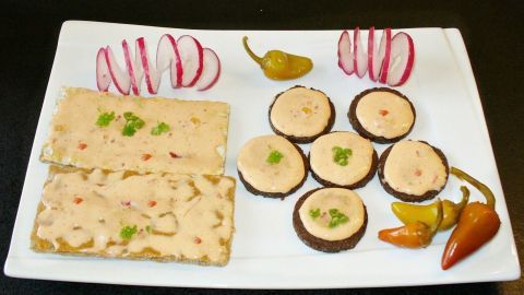 Ich liebe es besonders scharf: Über gekaufte Produkte mit Pfeffer oder Chili kann ich nur müde lächeln. Hier mein Rezept für feurigen sahnigen Streichkäse. Auf einem weißen Teller liegt feuriger Streichkäse in Form von runden und rechteckigen Scheiben, garniert mit Frischkäse und Paprika.