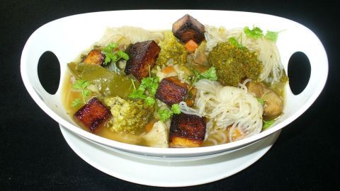Eine Schüssel mit knusprigem Räuchertofu und Konjaknudeln, umgeben von buntem Gemüse in einer klaren Brühe.