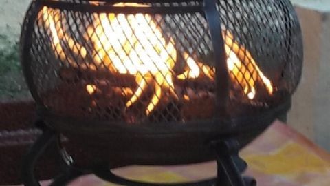 Ein Feuergestell spendet Wärme an einem kühlen Abend, umgeben von grünem Gras und einem bunten Tuch.