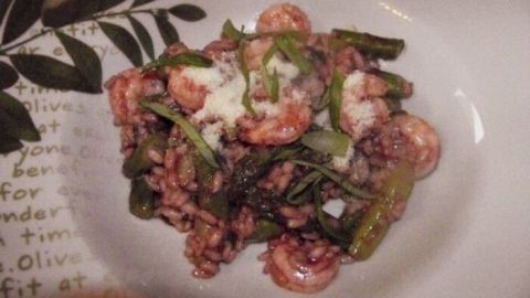 Ein cremiges Risotto mit Spargel und Garnelen liegt auf einem dekorierten Teller, umgeben von grünem Gemüse.