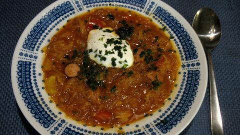 In einer tiefen Schüssel liegt eine dampfende Sauerkraut-Paprika-Suppe, garniert mit einem Löffel Sahne und frischen Kräutern.