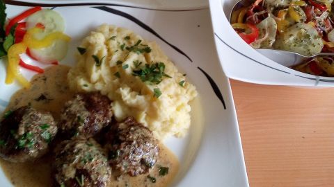 Zarte Minifrikadellen in Dijon-Senfsoße liegen neben cremigem Kartoffelpüree auf eleganten Tellern, umgeben von frischem Gemüse.