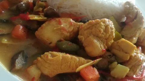 Ein Hähnchen-Curry mit buntem Gemüse wird zusammen mit Reis serviert, alles auf einem weißen Teller angerichtet.