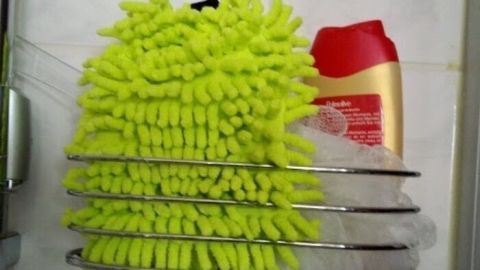 Ein flauschiger Putzhandschuh hängt in einer Duschablage, neben einer Flasche Duschgel, bereit für die Reinigung der empfindlichen Haut.