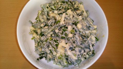 Ein frischer Schnittlauchsalat liegt in einer weißen Schüssel, umgeben von einer holzfarbenen Tischoberfläche.