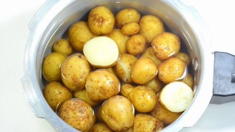 Eine Gruppe von ungekochten Kartoffeln liegt in einem Schnellkochtopf mit Wasser, bereit zum Garen.