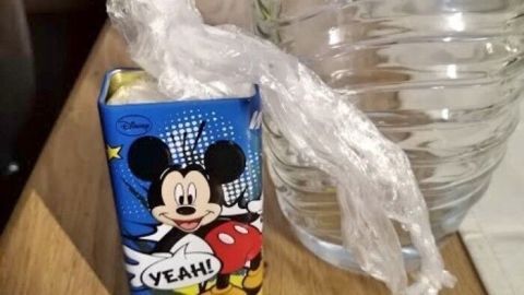 Eine Plastiktüte hält einen kleinen Saftkarton mit Mickey Mouse und dem Text "YEAH!" neben einer Glasflasche auf einem Tisch.