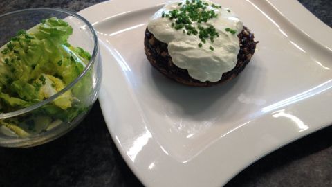 Gefüllte Champignons liegen auf einem weißen Teller, garniert mit Sahne und Schnittlauch, daneben ein Salat.