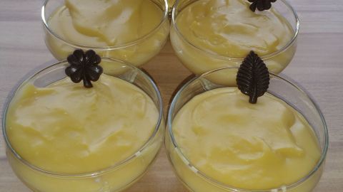 Drei Schalen mit cremigem Vanillepudding aus Soja-Vanillemilch, dekoriert mit Schokoladenblüten, stehen auf einem Holztisch.