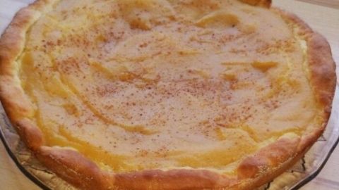 Ein goldbrauner Apfelmuskuchen mit Hefeteig liegt auf einem Glas-Teller und steht auf einer Holzoberfläche.