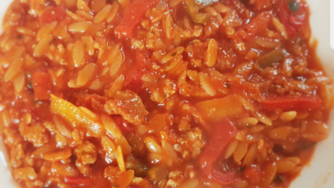 Ein gefüllter Teller mit Kritharaki-Nudeln, bedeckt von einer herzhaften Tomatensauce und buntem Gemüse, appetitlich angerichtet.