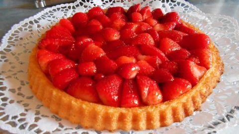 Eine Erdbeertorte mit glänzendem Guss steht elegant auf einer feinen, durchbrochenen Tortenschicht und sieht köstlich aus.