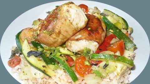 Feta gefülltes Schweinefilet liegt auf einer bunten Gemüse-Bett mit Zucchini, Tomaten und Kräutern, alles in einem Teller.
