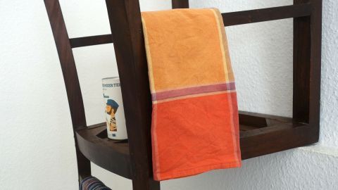 Ein Stuhl dient als Küchenregal mit Handtuchhalter, auf dem ein Handtuch und eine Dose stehen, vor einer Wand.