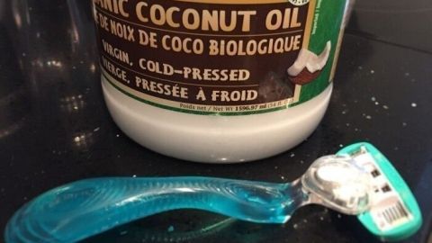 Ein Rasierer liegt neben einer offenen Dose mit Bio-Kokosnussöl auf einer dunklen Oberfläche, bereit zum Achsel rasieren.