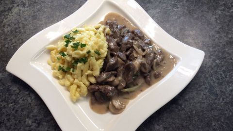 Ein Teller Boeuf Stroganoff liegt auf einer dunklen Oberfläche, umgeben von cremigen Nudeln und einer aromatischen Soße.