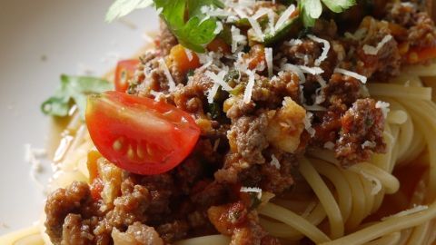 Ein Teller mit Spaghetti wird mit würzigem Haschee, frischen Tomaten und Kräutern garniert und wirkt appetitlich.