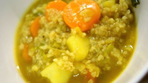 Der vegetarische Bulgur-Eintopf mit Karotten und Kartoffeln füllt eine weiße Schüssel, dampfend und bunt.