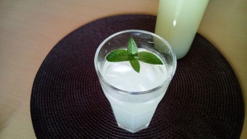 Ein frischer Ingwer-Zitronen-Drink in einem Glas mit Minzblatt, präsentiert auf einem dunklen Tischuntersetzer.