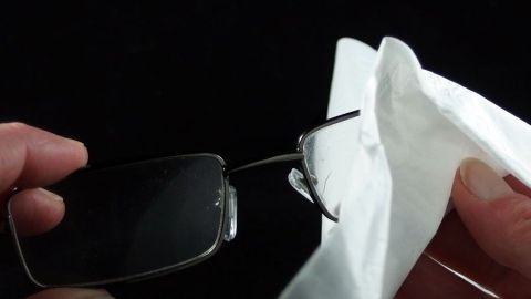 Brillengläser werden mit einem Tuch gereinigt, um streifenfrei zu sein, vor einem schwarzen Hintergrund.