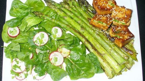 Frischer Spinatsalat mit Radieschen liegt neben grilliertem Spargel und gefüllten Tofuwürfeln auf einem weißen Teller.