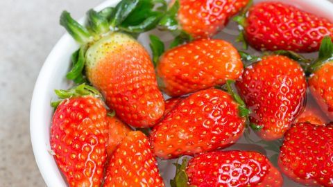 Frische Erdbeeren schwimmen in einer Schüssel mit Wasser und werden gründlich gewaschen, um Schmutz zu entfernen.