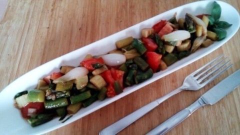 Ein bunter Spargel-Rhabarber-Salat wird auf einem langen weißen Teller serviert, umgeben von Besteck auf einem Holzuntergrund.